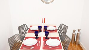 A dining table set with plates, cutlery, and blue glassware, surrounded by mesh chairs.