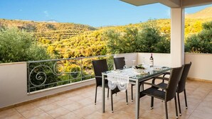 A balcony with a table set for two, overlooking a hilly landscape with trees and shrubs. - Kitries Summer Getaway - Eden Cozy Suite (Kitries)