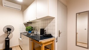 A compact kitchen with white cabinets, a black countertop, a sink, a fan, and a small wooden table. - Kitries Summer Getaway - Eden Sandy Suite (Kitries)