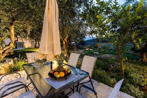 An outdoor dining area with a glass table, chairs, and a fruit bowl.
