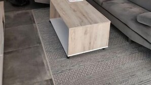 A modern living room with a sectional sofa, a wooden coffee table, a floor fan, and a wall-mounted abstract art piece. - Beautiful new house close to beaches and shops (Saint-Georges-d'Oléron)