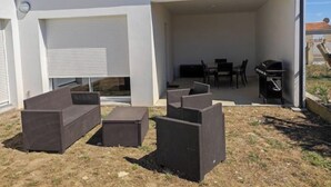 A covered outdoor patio with a dining table and chairs, a grill, and a sofa set. - Beautiful new house close to beaches and shops (Saint-Georges-d'Oléron)