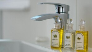 Ett badrum med en modern kran och tre flaskor schampo och balsam från märket Goldcrest, placerade på en vit hylla.