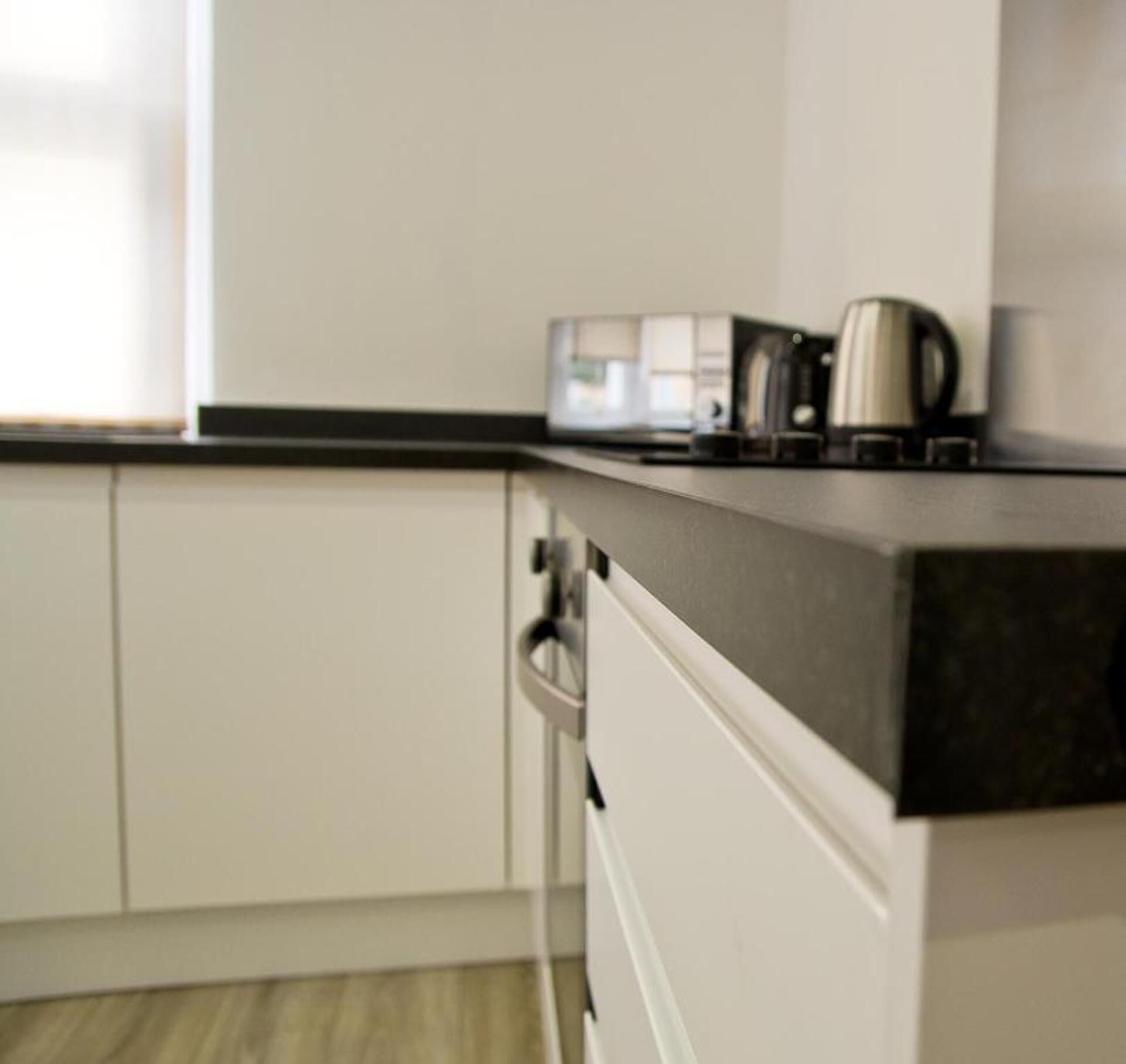 A kitchen with white cabinets, a black countertop, and a coffee maker.