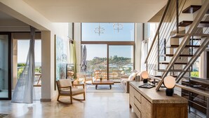 Un vaste espace de vie doté d’une grande fenêtre, d’un escalier en bois et d’un coin repas offrant une vue sur le paysage.