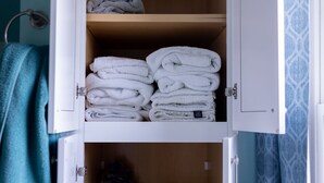 Ein Badezimmer mit einem weißen Schrank, der gefaltete Handtücher, ein blaues Handtuch und Toilettenpapier enthält.