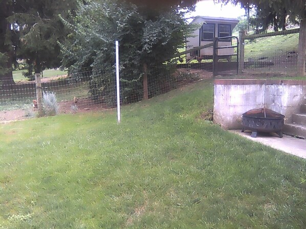 A grassy outdoor area with a metal fence, a concrete structure, and a metal fire pit.