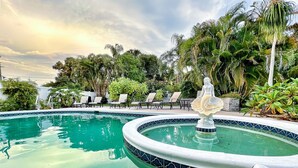 Una piscina amb una font decorativa, envoltada de gandules i plantes tropicals.