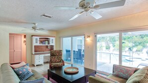 A living room with a sofa, armchair, and coffee table, a bookshelf, and a sliding glass door leading to an outdoor patio. - Fun Getaway in the Sun Private Saltwater Pool Yard (Gulfport)