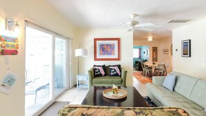 A living room with a green sofa, a light blue sofa, a coffee table, and a ceiling fan. There is a dining area in the background with a table and chairs. - Fun Getaway in the Sun Private Saltwater Pool Yard (Gulfport)