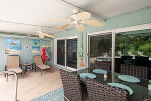A sunlit patio with wicker furniture, ceiling fans, and a glass door leading to a pool area. - Fun Getaway in the Sun Private Saltwater Pool Yard (Gulfport)
