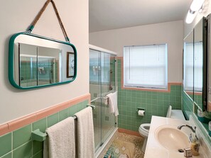 A bathroom with a glass shower, a sink, a mirror, and a window with blinds. - Fun Getaway in the Sun Private Saltwater Pool Yard (Gulfport)
