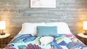 A bed with a floral bedspread, a single pillow, and a framed artwork on a wooden wall. - Fun Getaway in the Sun Private Saltwater Pool Yard (Gulfport)