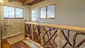 A wooden railing with a unique design, a wooden ceiling, and two windows with blinds.