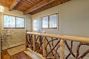 A wooden railing with a unique design, a wooden ceiling, and two windows with blinds.