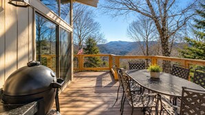 Una terraza con parrilla, mobiliario exterior y vistas a montañas.