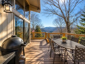A deck with a grill, outdoor furniture, and a view of mountains.