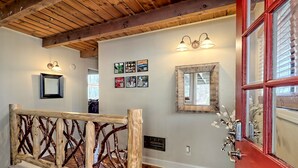 A wooden staircase with a rustic railing, a red door with glass panels, and wall-mounted light fixtures.
