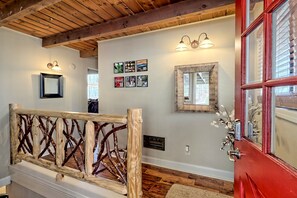 A wooden staircase with a rustic railing, a red door with glass panels, and wall-mounted light fixtures.