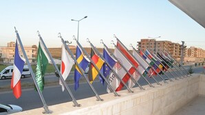 Una fila de banderas en una pared, con edificios y una calle al fondo.