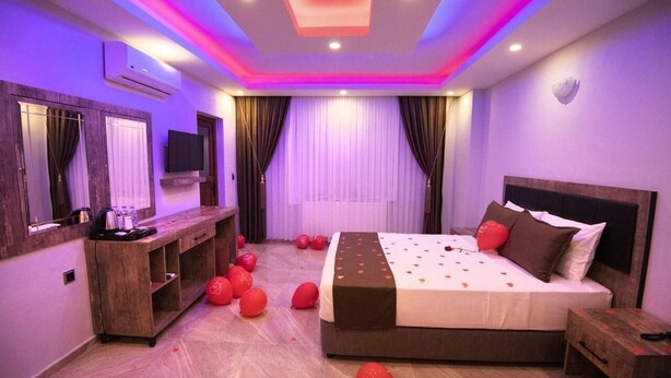 Un dormitorio moderno con una cama grande, una consola de madera, un televisor de pantalla plana e iluminación LED en el techo.