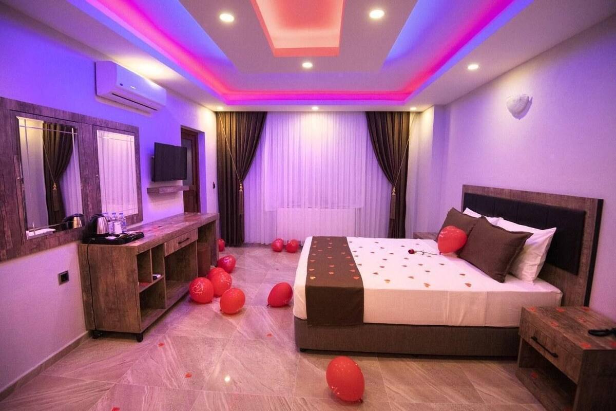 Une chambre moderne avec un grand lit, une console en bois, un téléviseur à écran plat et un plafond doté d’un éclairage à LED.