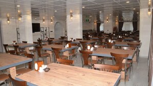 Un comedor amplio con varias mesas y sillas, techo alto con diseños tipo cuadrícula y lámparas fijadas a la pared.