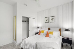 A bedroom with a bed, two bedside tables, a wardrobe, and a door leading to another room.