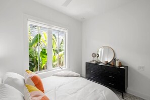 A bedroom with a bed, a dresser, a mirror, and a window with a view of greenery.