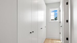 Un pasillo con paredes blancas, piso de madera y ventana con vista al cielo.