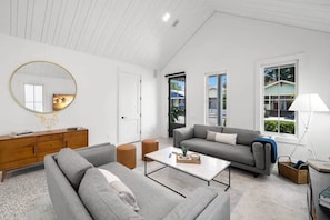 A modern living room with a grey sofa, a coffee table, and a wooden cabinet. - Xavier at Angels Quarter | Rooftop Terrace (Tampa)