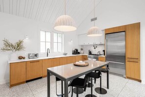 A modern kitchen with wooden cabinets, a stainless steel refrigerator, and pendant lighting. - Xavier at Angels Quarter | Rooftop Terrace (Tampa)