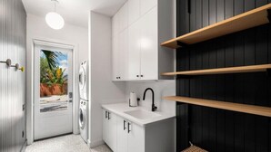 Cocina compacta con gabinetes blancos, encimera negra y vista a una palmera.