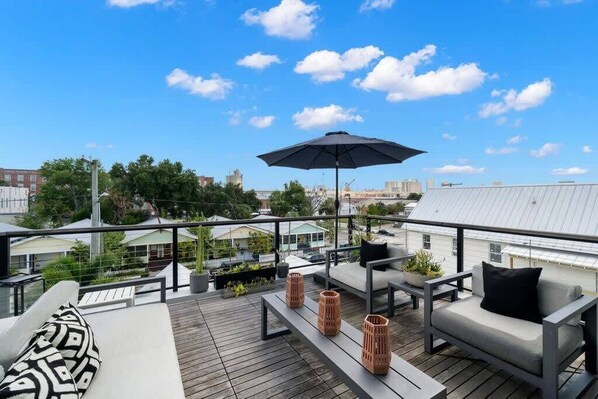 A rooftop terrace with outdoor seating, a large umbrella, and a view of the cityscape.