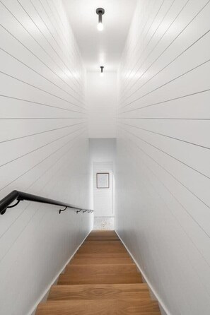 A narrow, white-paneled hallway with a wooden floor and a handrail on the left. - Xavier at Angels Quarter | Rooftop Terrace (Tampa)
