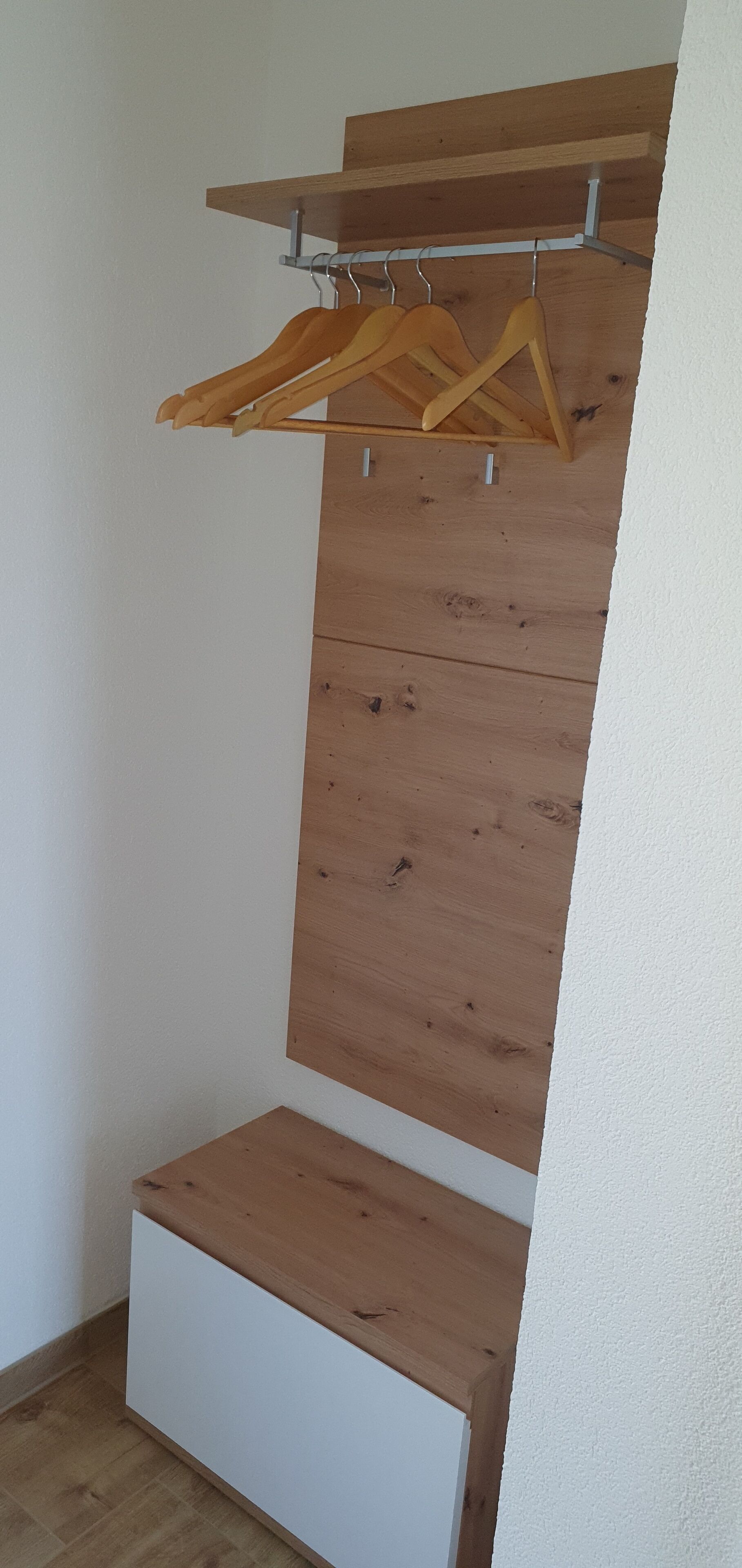 Huoneessa on puinen vaatekaappi, valkoinen kaappi ja puinen hylly.