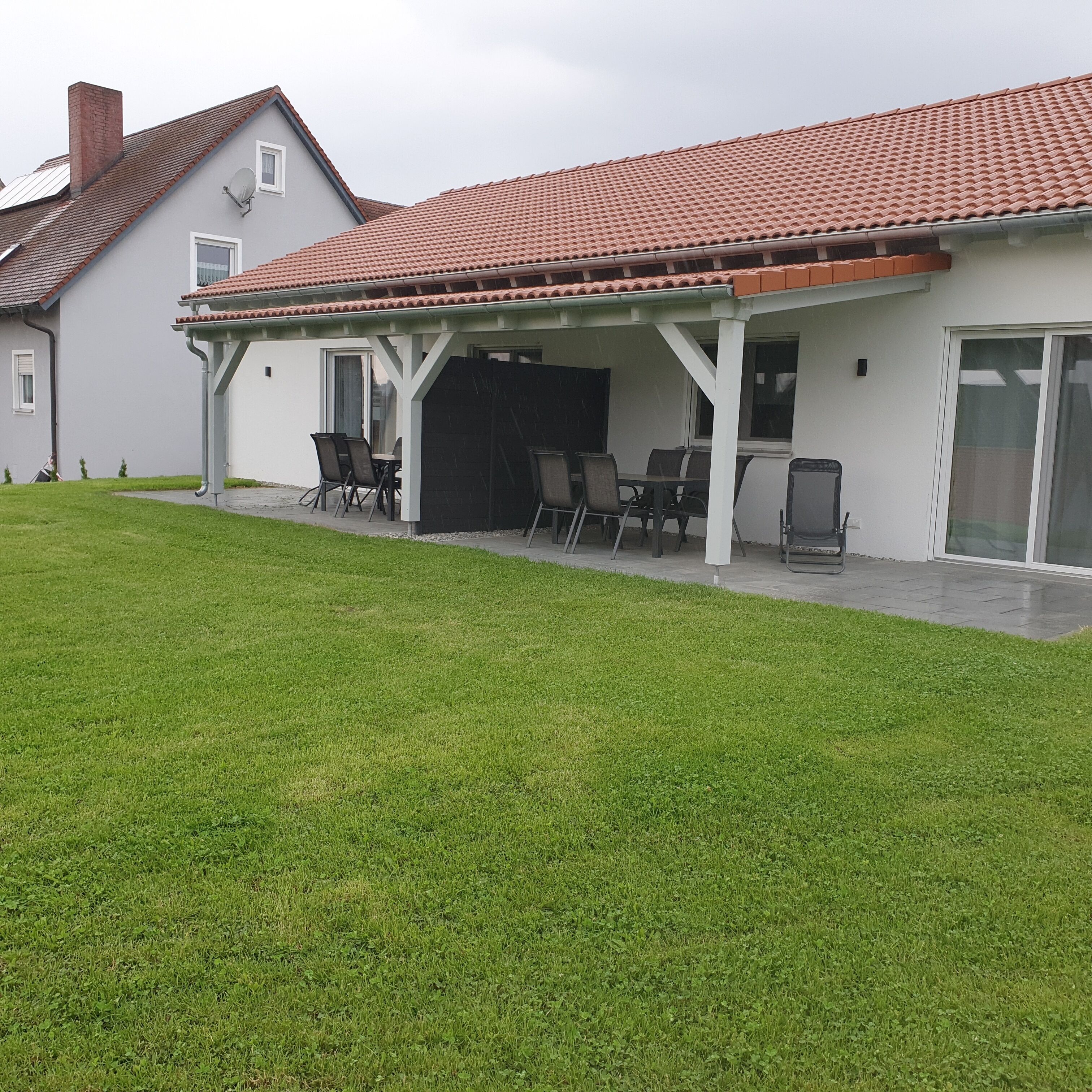A house with a covered patio area, a lawn, and a red-tiled roof.