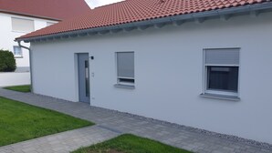 A modern two-story house with a red-tiled roof, white exterior walls, and a small front yard with a paved walkway. - Vacation apartments Hesselperle (Gerolfingen)