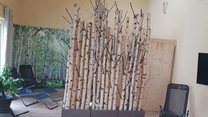A room with a birch tree installation, two lounge chairs, a potted plant, and a wooden panel on the wall. - Vacation apartments Hesselperle (Gerolfingen)