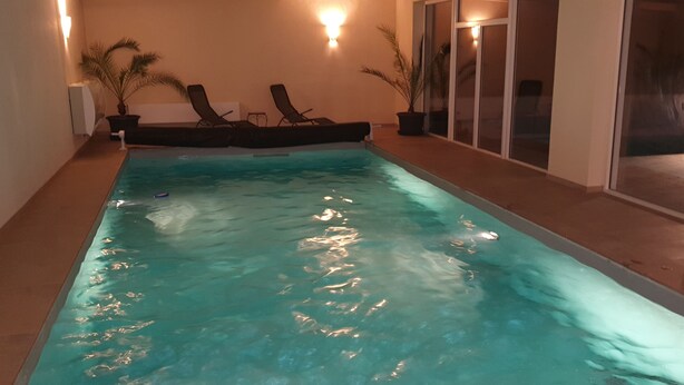 An indoor swimming pool with clear water, lounge chairs, and potted plants. - Vacation apartments Hesselperle (Gerolfingen)