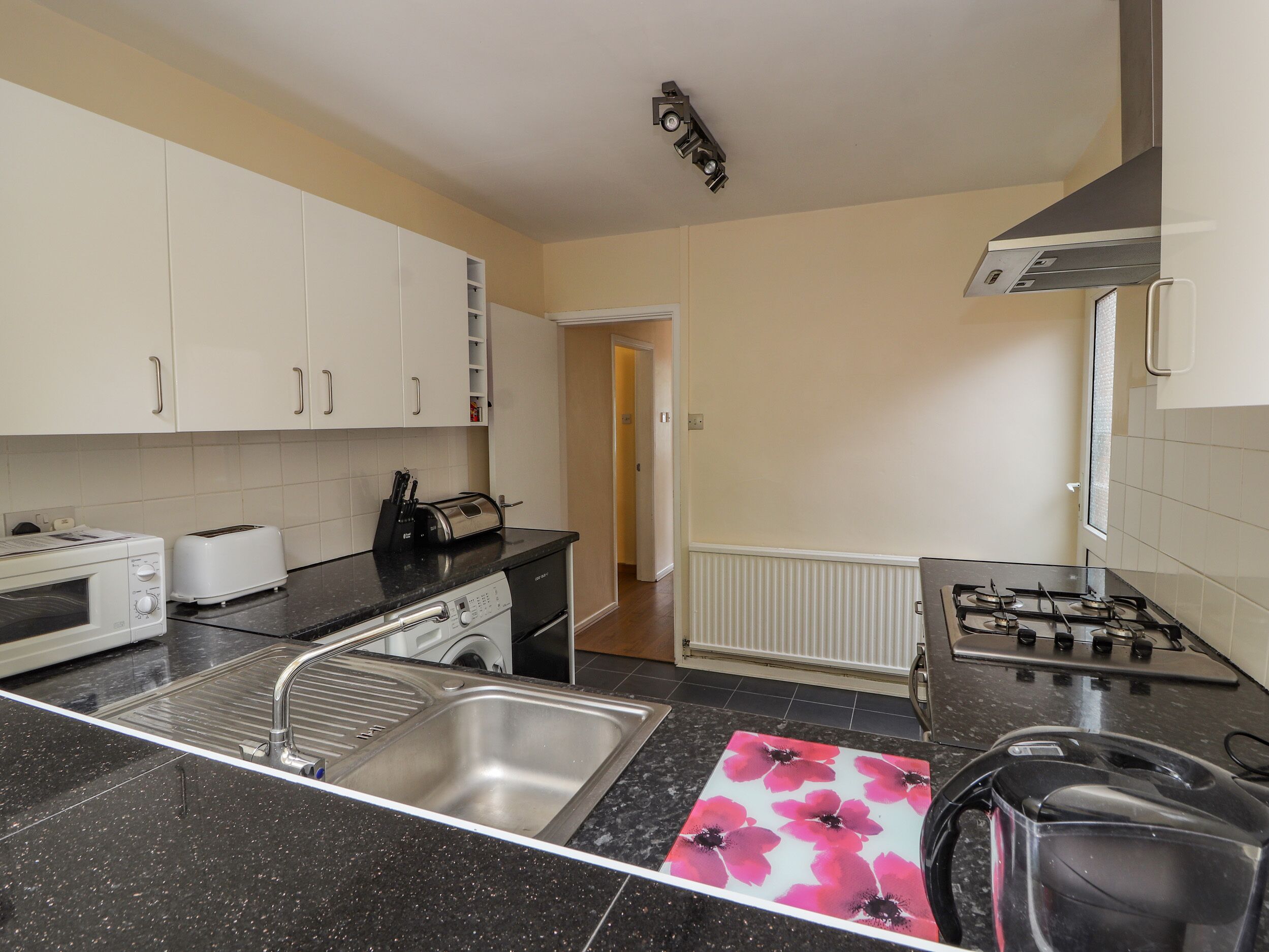 A compact kitchen with white cabinets, a black countertop, a stainless steel sink, a toaster, a kettle, and a gas stove.