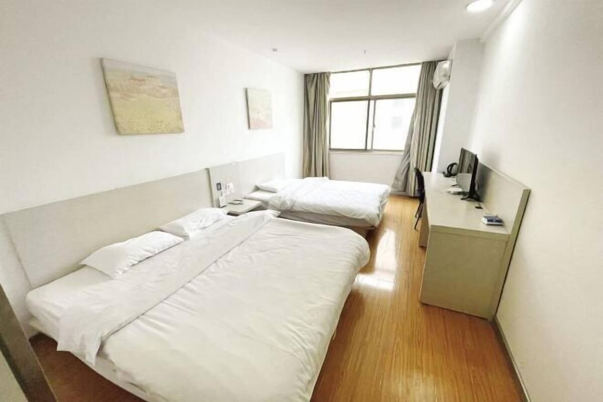 A hotel room with two beds, a desk, a chair, a TV, and a window with curtains.