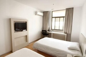 Een hotelkamer met twee bedden, een televisie, een bureau en een raam met gordijnen.