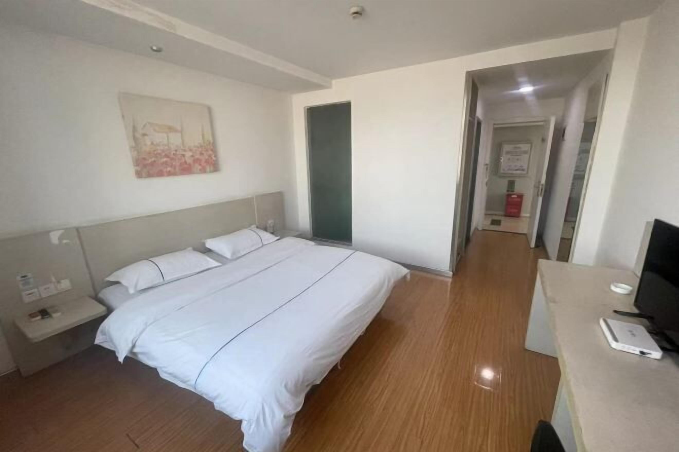 A hotel room with a bed, bedside table, TV, and a painting on the wall.