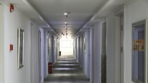 Un largo y estrecho pasillo de hotel con puertas a ambos lados, un detector de incendios a la izquierda y un cartel en la pared derecha.