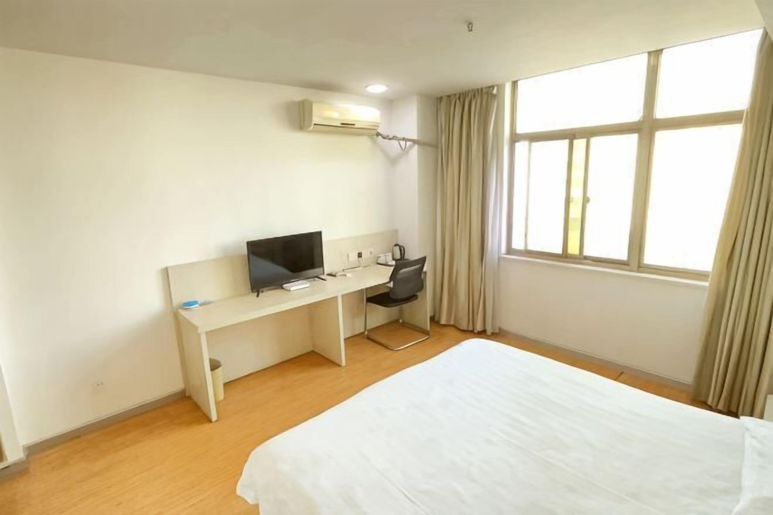 A hotel room with a bed, a desk with a computer, a chair, and a window with curtains.
