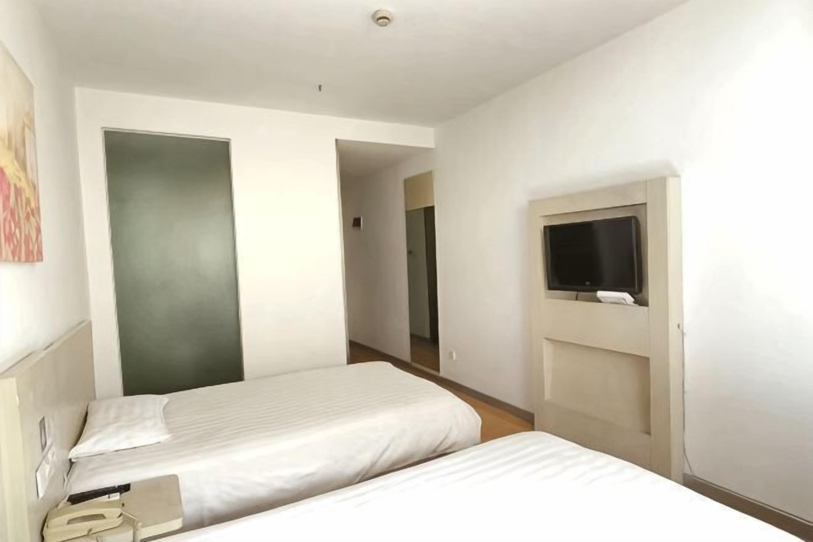 A hotel room with two beds, a television, and a door leading to another room.