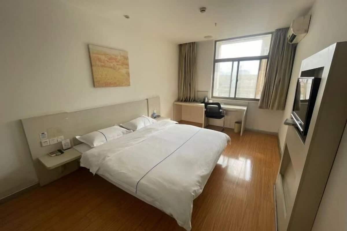 A hotel room with a large bed, a desk, a chair, and a window with curtains.