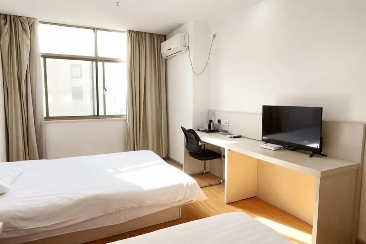 A hotel room with a bed, a desk, a chair, a television, and a window with curtains.