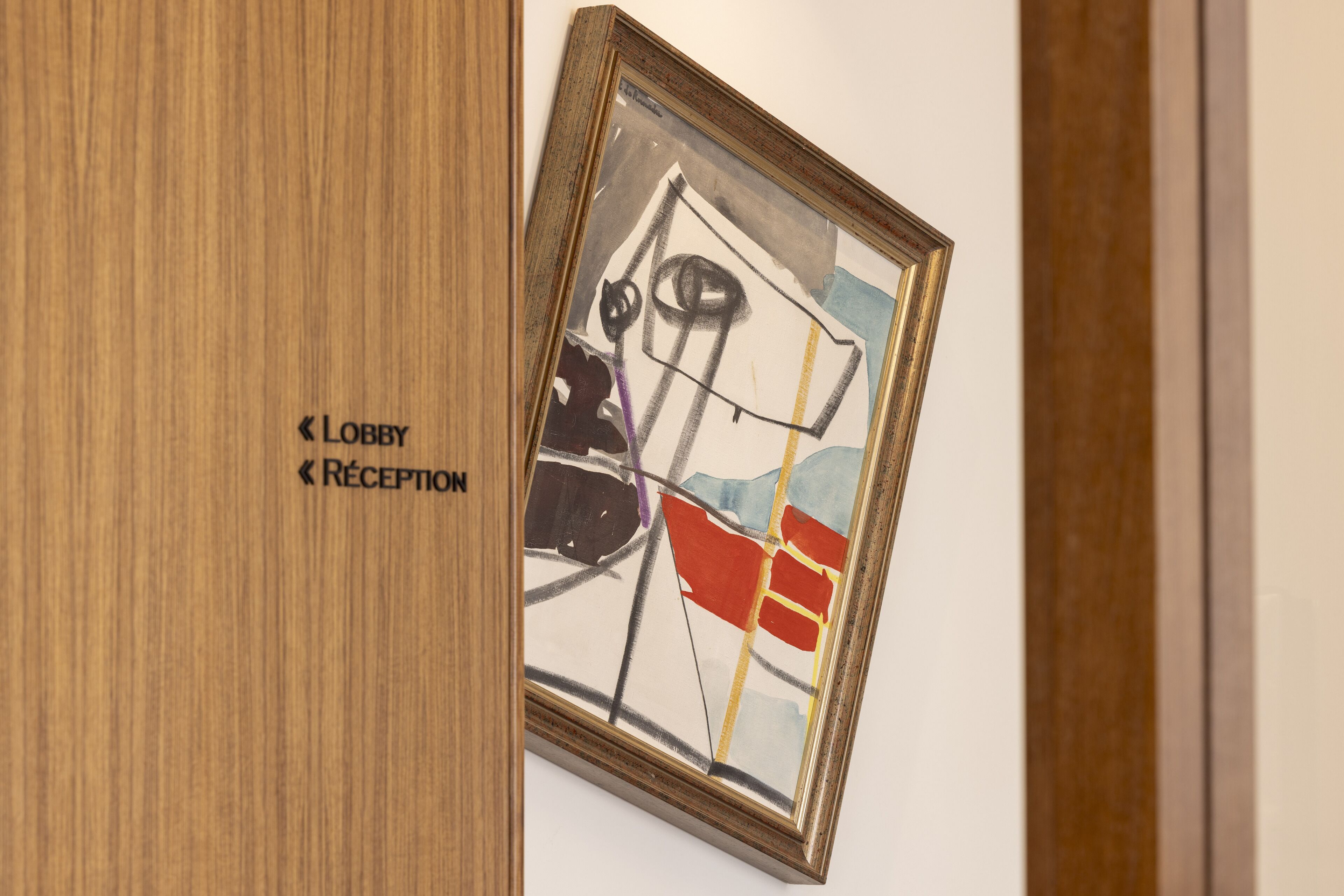 A framed abstract painting in a lobby area with directional signs for 'Lobby' and 'Reception'.